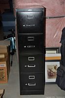 Tall black metal filing cabinet with four drawers and silver handles and label holders.