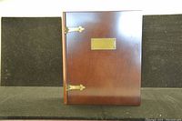 Closed cherry finish wood memory box with brass fittings, showing the front with brass plaque and hinges.