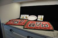 Photo showing six quilted vintage Christmas placemats, three packages of cocktail napkins, and an oval cookie tray arranged on a black surface.
