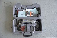 Opened plastic case showing Dremel finishing sander, sanding accessories, and manuals inside the compartment slots.