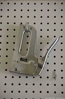 Heavy duty all metal work stapler photographed hanging on pegboard, showing silver metal construction and lever handle.