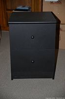 Front view of black 2 drawer cabinet showing closed drawers and simple round knobs.