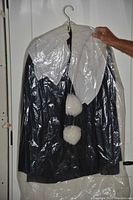 Front view of the Pierrot costume in a plastic garment bag showing white pointed collar and two pom poms on black fabric.