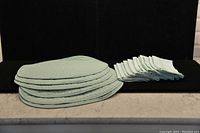 Six stacked light green placemats next to twelve folded matching light green cloth napkins on a flat surface.