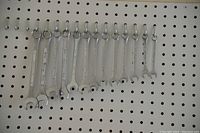 Photo of 12 metal combination wrenches hanging on pegboard hooks, showing open and box ends, various sizes.