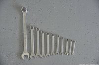 Photo showing 11 combination wrenches arranged in descending length and size on a speckled grey floor surface.
