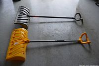Photo showing two ergonomic handle snow shovels lying on a concrete floor.