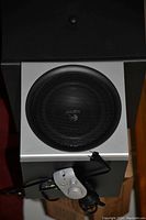 Photo showing a silver Logitech subwoofer with a black speaker grille, a wired audio controller with dial and buttons attached by cable.