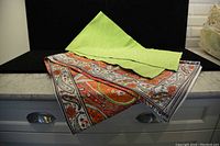 Image of the paisley tablecloth and solid green table runner displayed on a surface against a black background