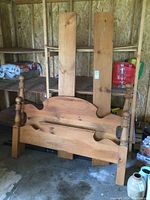 Front view of the assembled headboard and footboard of the solid pine four poster queen bed frame leaning against a plywood wall inside a garage.
