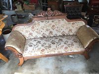 Full view of antique settee showing solid wood frame and floral fabric upholstery in cream, pinks, and greens.