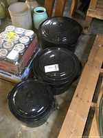 Three black enamel canning pots with lids arranged on the floor, showing varying sizes and matching lids.