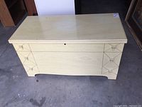 Frontal view of the vintage cedar lined chest showing cream color, geometric front design, keyhole, and overall shape.