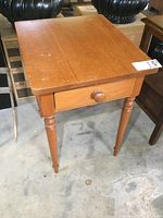 Front view of a solid wood rectangular end table showing top surface with minor scuffs and drawer with round knob.