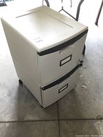 White resin 2-drawer filing cabinet viewed from the front and top corner showing two drawers, handles, label holders, and keys on the side.