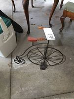 Full side view of the metal high wheel bike decor showing large front wheel and smaller rear wheel with wooden handle and seat.