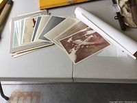 The full set of military aircraft photos spread out on a table including a rolled poster tube and Kodak paper box.
