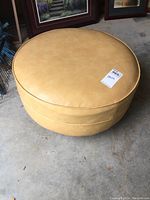 Top view of the round vintage rolling ottoman showing smooth tan upholstery and price tag.