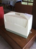 White plastic carrying case closed, rectangular with handle on top and green base.