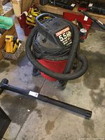 Full view of Craftsman shop vacuum with hose wrapped around top, showing red tank, black top and hose, with one large nozzle attachment lying on floor.