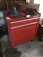 Front and top view of red Waterloo rolling tool cabinet with two drawers and a bottom compartment, placed on concrete floor, showing some power tools on top that are not included.