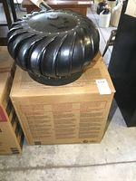 Two photos showing individual black turbine roof vents placed on cardboard boxes. One vent is complete with base, the other lacks it.