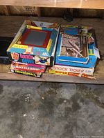 Stack of vintage board games including Etch A Sketch on top, Battleship, Thunderball, Hands Down visible on middle boxes, Stock Ticker and Super Spiral Race partially visible on bottom box.