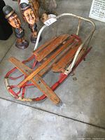 Side angle view of vintage kids wooden and metal sleigh with red runners and white handlebar, showing aged wear.