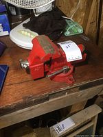 Front and side view of the red Sears 3.5-inch bench vise with clamp handle and rotating base, mounted on a wooden bench, showing condition and wear.
