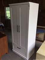 Front view of white wardrobe cabinet showing two shaker-style doors and bottom drawer
