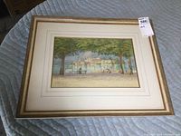 Framed watercolour painting showing overall lot condition and size, with trees and village by water