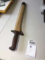 Sheathed bayonet with wood handle visible, MaxSold tag present