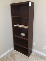Full view of the tall dark wood bookshelf showing multiple shelves and some papers placed on mid shelf.