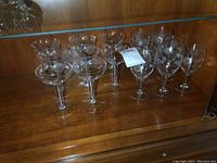 Full set of 15 Cornflower stemware glasses on wooden surface inside display cabinet, showing variety and hollow stem glasses.