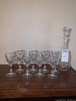 Photo showing the full set of 8 crystal glasses and the crystal decanter with stopper on a wooden surface against a plain wall.
