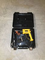 DeWalt drill inside open black carrying case, showing yellow drill body, coiled cord, and separate side handle attachment.