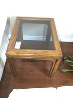 Photo of one wood end table showing natural wood finish and smoked glass panel on top surface, angled side view.