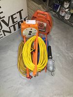 Overview of cord reels with yellow cords and handheld trouble light on concrete floor.