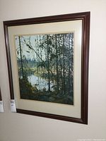Framed print showing forest landscape with river scene visible through dense black silhouettes of tree branches and trunks against a blue-gray background.