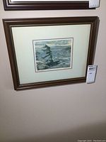Framed print in dark wood frame hung on wall, showing entire print with matting and partial view of artwork.