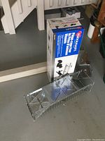 Large metal live animal cage trap with box showing Havahart branding and packaging in background, cage laid on floor.