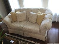 Full front view of the cream damask Kroehler loveseat with four cushions, positioned near window with sheer curtains.