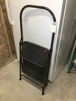 Front view of folded metal two-step ladder leaning against a wall.