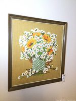 Full view of needlepoint artwork showing bouquet of sunflowers and daisies in woven basket, framed.