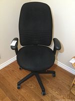 Front view of black fabric office chair showing padded seat, backrest, and armrests. Chair base with caster wheels visible.
