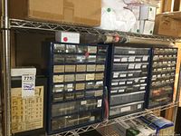 Photo of four large metal and plastic drawer organizers on metal shelving filled with labeled hardware and electrical components