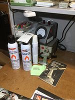 Photo showing two Emzone butane fuel cans, a small torch, instruction booklet, cleaning cloth, and a vintage electrical power supply with ammeter.