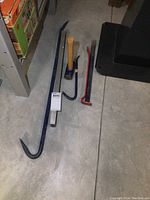 Photo showing three pry bars, large hammer, and level on concrete floor.