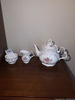 Full view of tea set showing teapot, creamer, and sugar dish on wooden table with clear view of floral patterns and gold trim