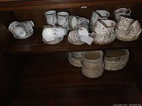 Photo showing teacups, saucers, double handled cups, coffee mugs, and stacked plates in dark wood cabinet.